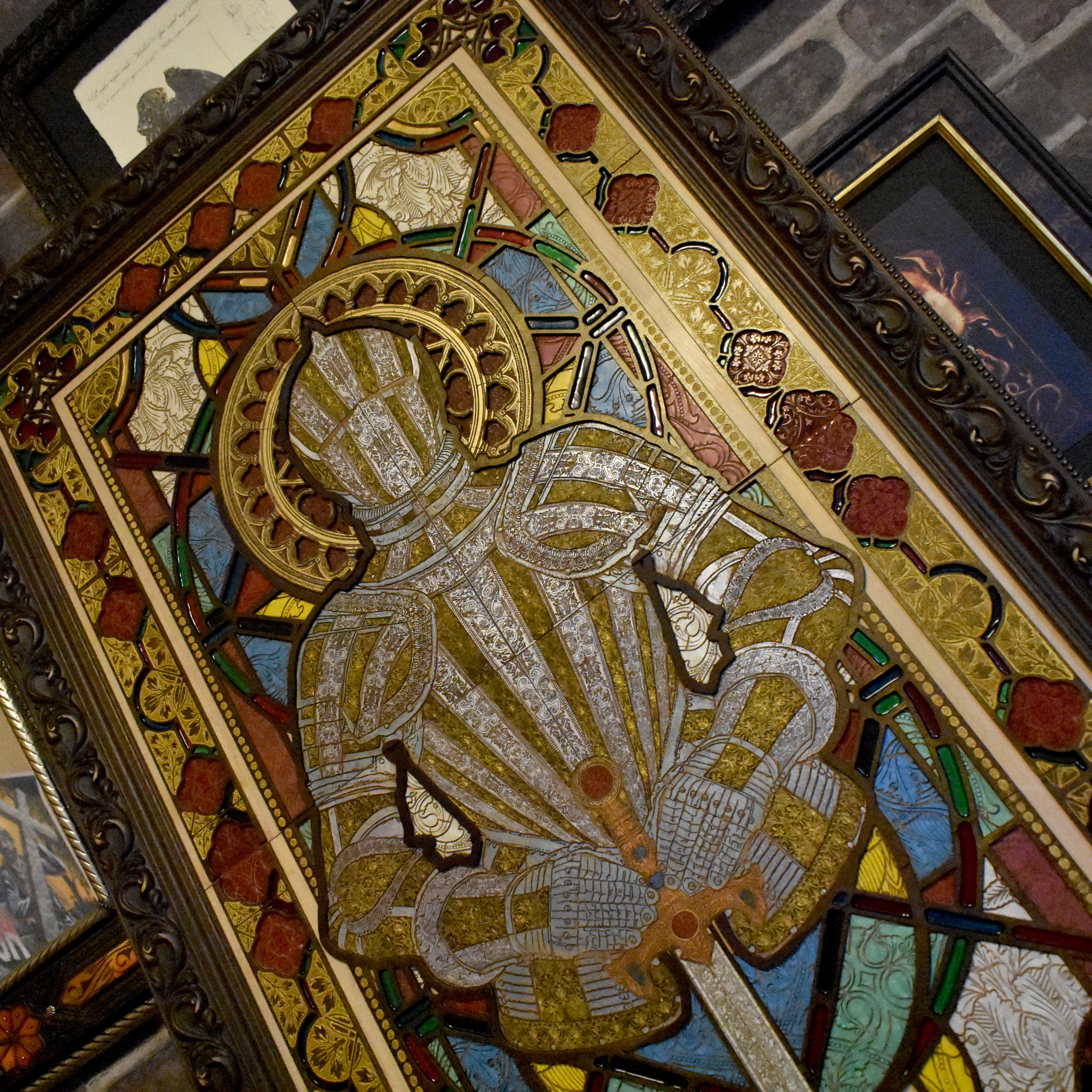 Handcrafted wooden artwork featuring a medieval knight in armor, recreated as a gothic stained glass window design. Made from solid maple wood, hand-painted with acrylic vitrail paint, and framed in a dark brown flourish frame.

