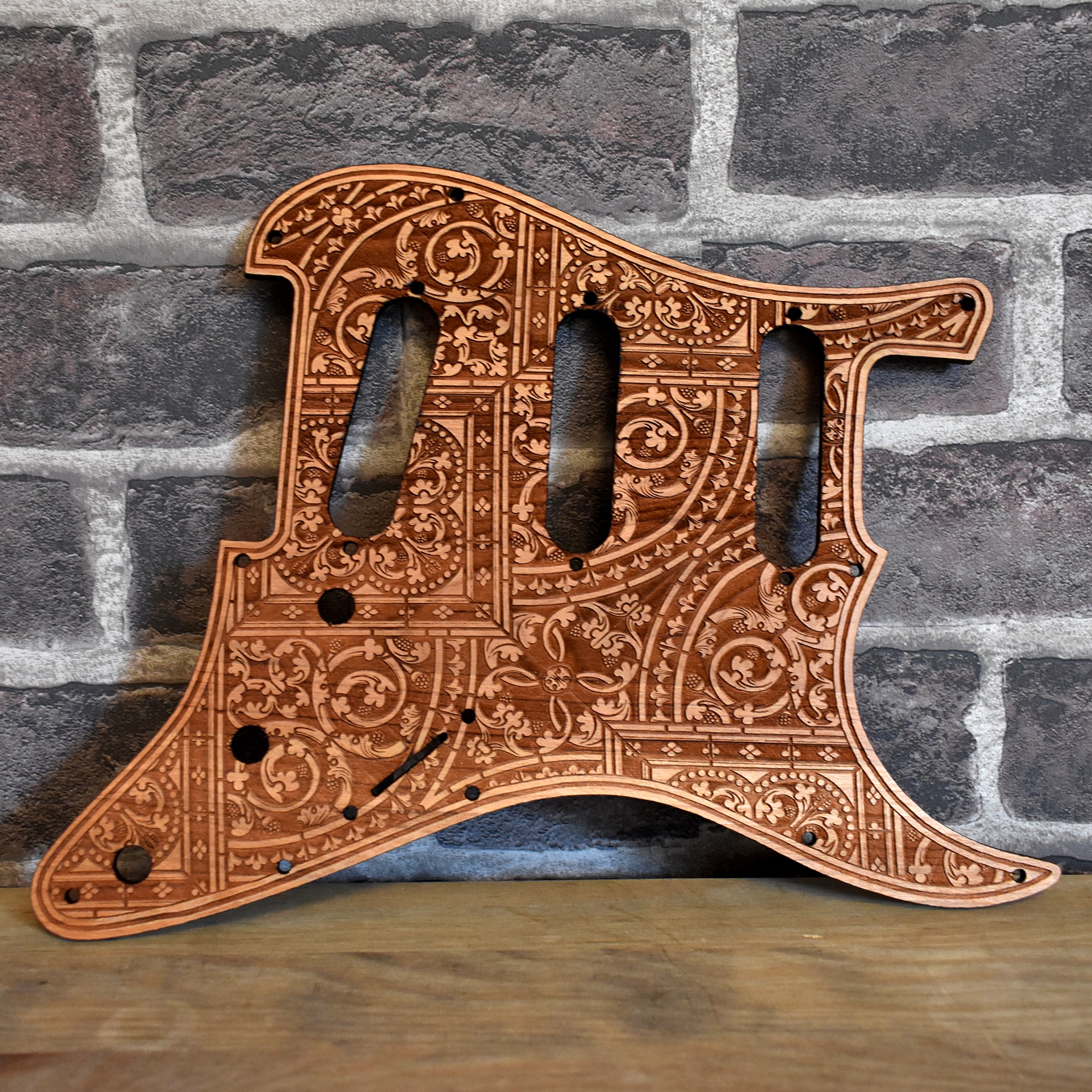 Front view of handcrafted cherry wood pickguard with laser-engraved flourish design for Fender Stratocaster